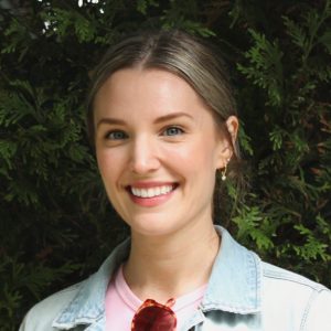 Caroline Anderson, wearing a jean jacket with a pink shirt smiling in front of a tree