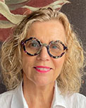 Portrait photo of Gabe Morrison. Gabe has shoulder-length blonde hair and is wearing tortoise shell glasses, and a white blouse.