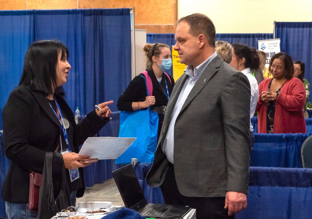 A B.Ed. student and exhibitor chat at a job fair booth