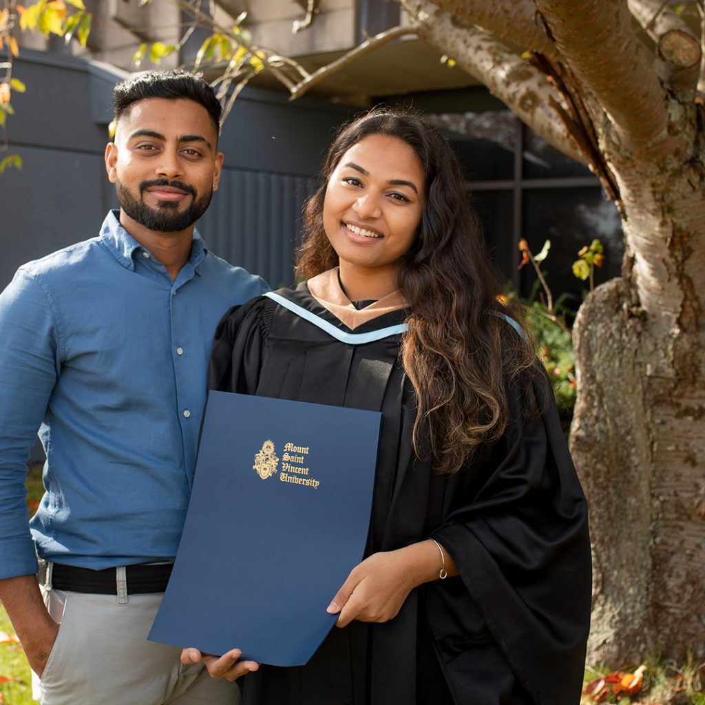 BBA graduate standing outside of Seton with degree and another person.