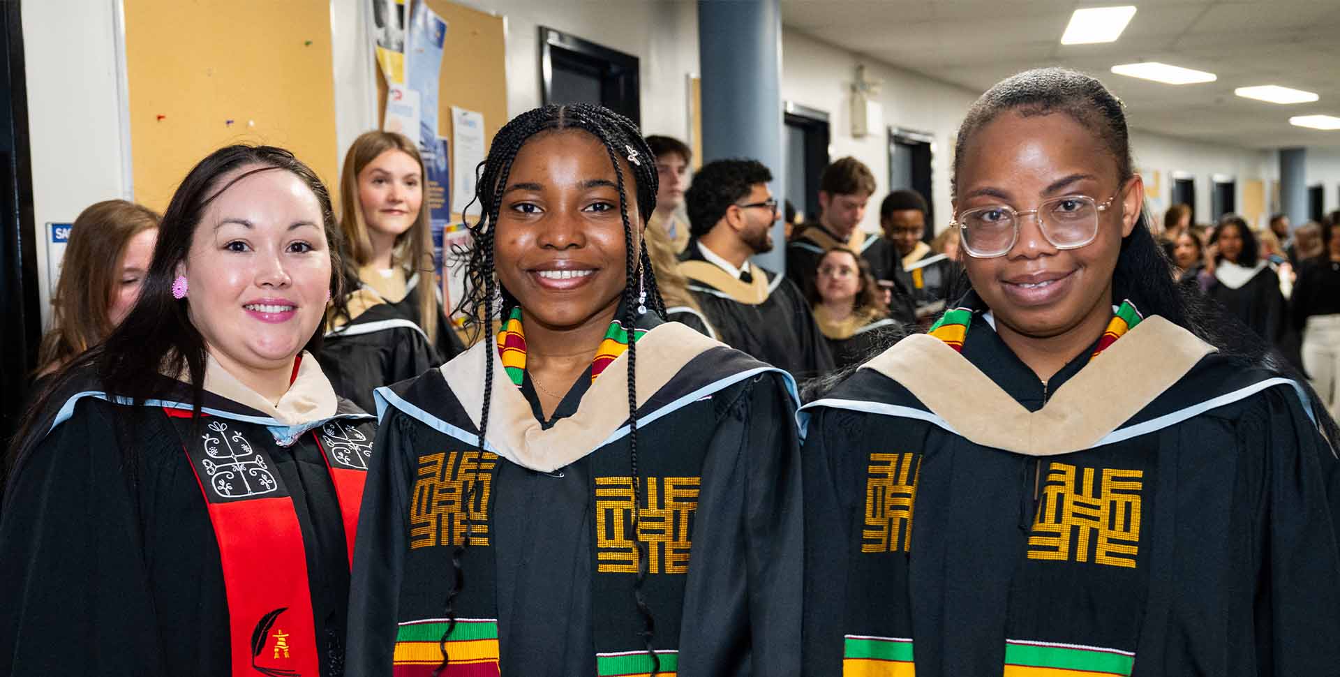 Three graduating business administration female students standing in the hall, smiling at the camera before walking into the auditorium for the spring 2026 convocation ceremony.