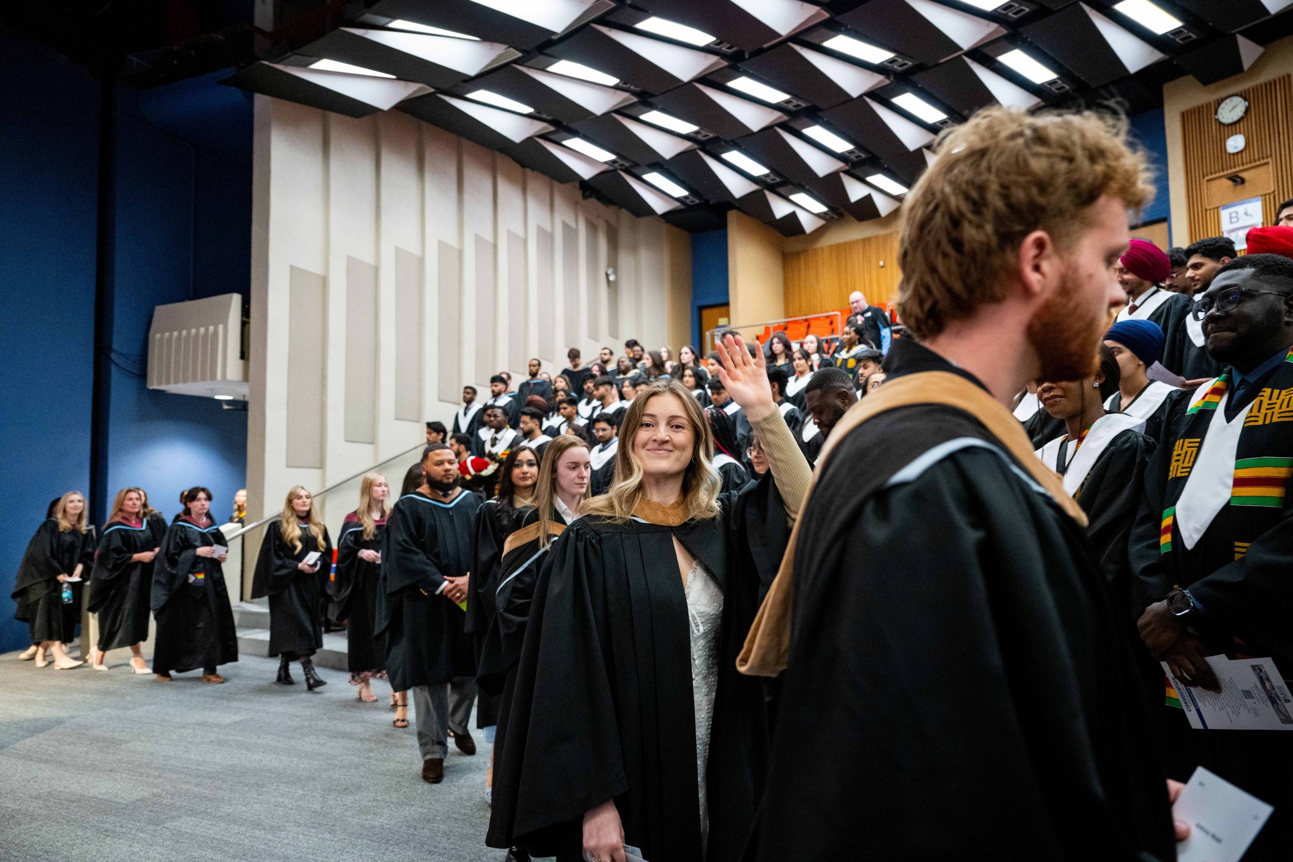 MSVU business administration students walking into the auditorium at the spring 2026 convocation ceremony. One female is waving and smiling at her friends or family. 