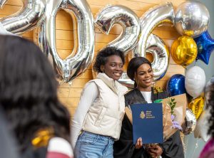 Student at the spring 2026 graduation ceremony reception standing with another person in front of the 2026 balloon display. 