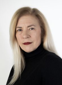 Headshot of Alison Jordan George Gray SKAL Award winner. Alison is a white woman who has long blond hair and is wearing a black turtleneck. She is standing in front of a white background.