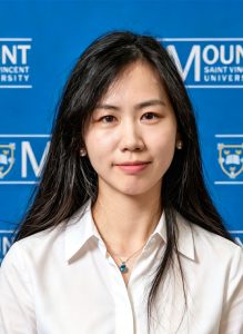 Headshot of Lei Liu 2026 Business and Tourism International Student of the Year award winner at MSVU. Lei is an Asian woman with long dark hair, a white shirt and is standing in front of a blue background with the Mount logo. And she is smiling.
