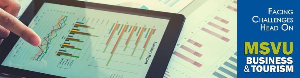 This is a photo of a tablet on a table with three different kinds of graphs on it and a hand pointing at the last graph. Under the tablet are papers with more graphs and line charts.