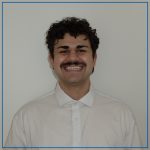 Photo of Justin Jackson. Justin is a male student who is wearing a white button up shirt, he has a mustache and short curly hair and has a huge smile.