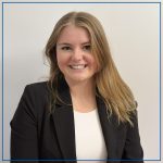 Photo of Keira McInnis. Keira has long blond hair, is wearing a dark suit coat with a white shirt underneath and is smiling at the camera.