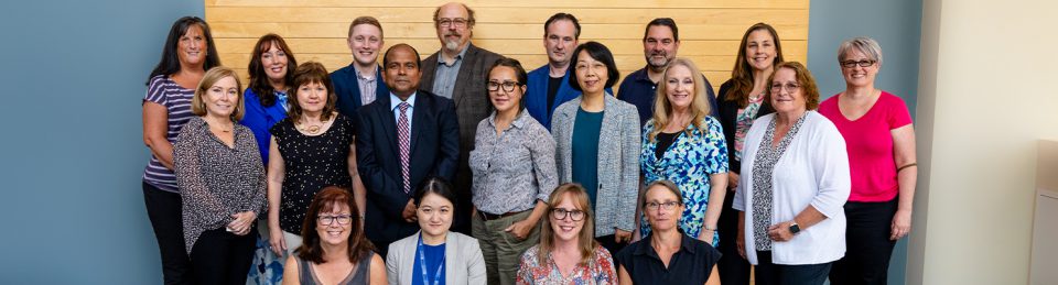 A group photo of most of the faculty of the business and tourism department. Three rows of people, 8 in the back row, 7 in the middle row and 4 in the last row. Photo taken in the McCain lobby in September. Everyone is smiling.