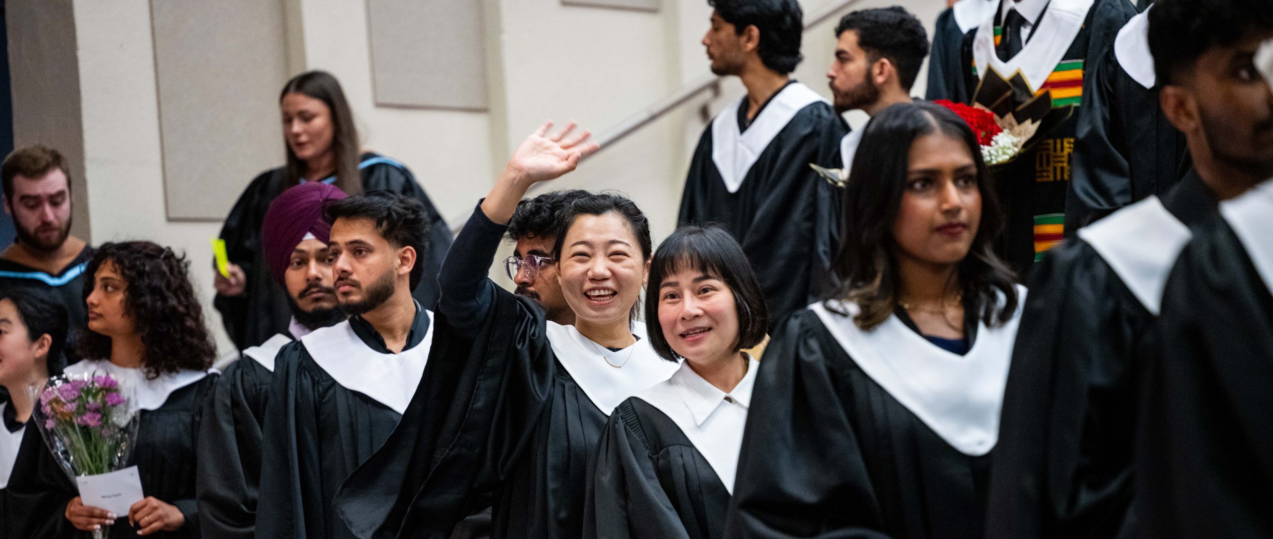 Tourism and Hospitality Management diploma students entering the auditorium during the May 2026 convocation ceremony. One female student waving at what is probably her family and friends and smiling.