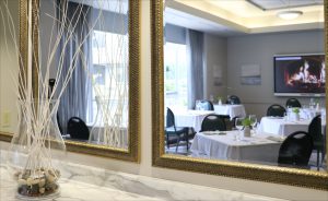 Photo of restaurant dining area through mirrors trimmed in gold. There is a fancy ornamental plant in the foreground. 