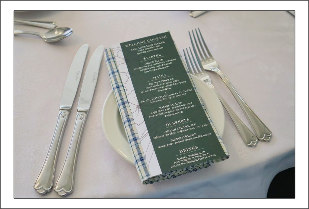 The Mount's Tourism and Hospitality Management student kitchen which is called Vincent's Restaurant. Photo of a forest green menu on a plate between knives and forks on a table with a tablecloth. 