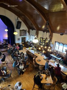 Students enjoying lunch at Church Street Brewery – Wolfville. This is a view from a balcony looking down on the restaurant. Very pretty place with a light coloured bar and tables and a large purple stained glass window to the left of the photo. 