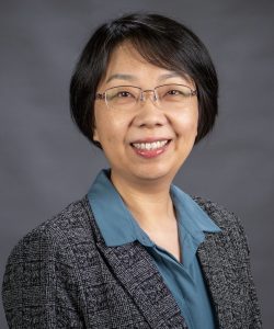 Headshot of Dr. Tianyuan Yu, MSVU business and tourism department full time faculty member. Tian is an Asian woman with short dark hair, glasses, A huge, lovely smile and is wearing a grey blazer and a blue dress shirt. 