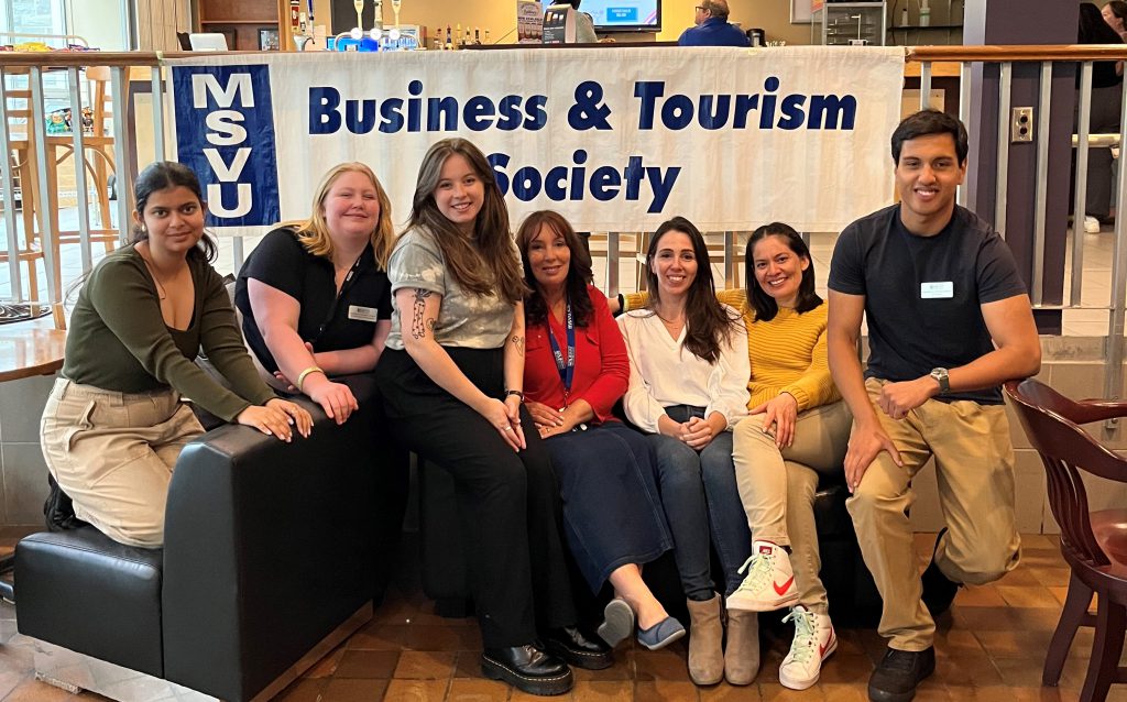 Business and Tourism society executive with faculty support person Maria Matthews sitting on a couch in the Rook during the pizza social. 2023 