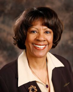 Retired Judge Corrine Sparks, wearing a brown jacket with a silver necklace and smiling at the camera.