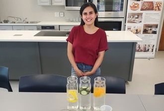 A student in a food lab standing in front of various drinks and meals