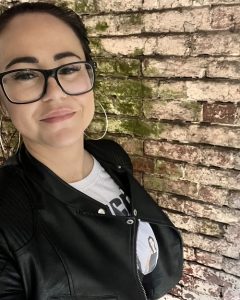 Ash Averly wearing a black leather jacket and posing against a brick wall