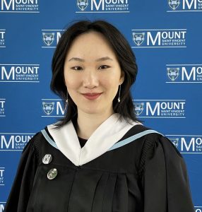 Helen Yao, wearing Convocation attire and standing in front of a MSVU backdrop