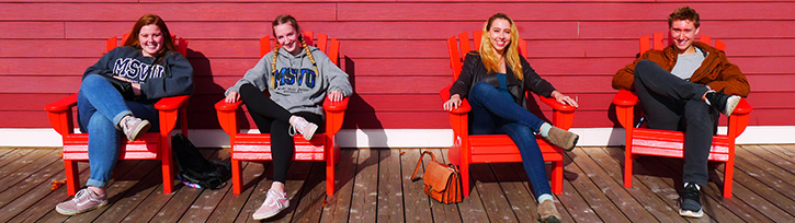 4 business and tourism students sitting in Adirondack chairs on a patio during one of the sustainable business tours.