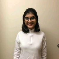 Janhvi - a brown woman wearing a white half zip sweater and glasses