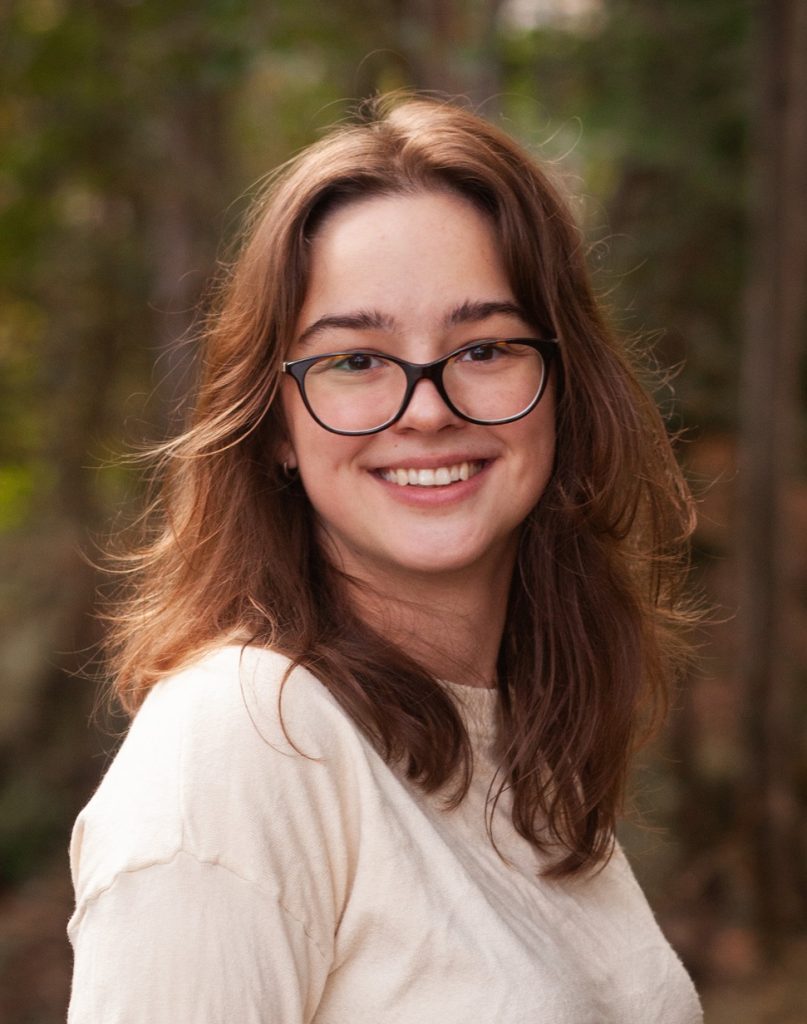 A woman with short brown hair and glasses smiles into the camera.