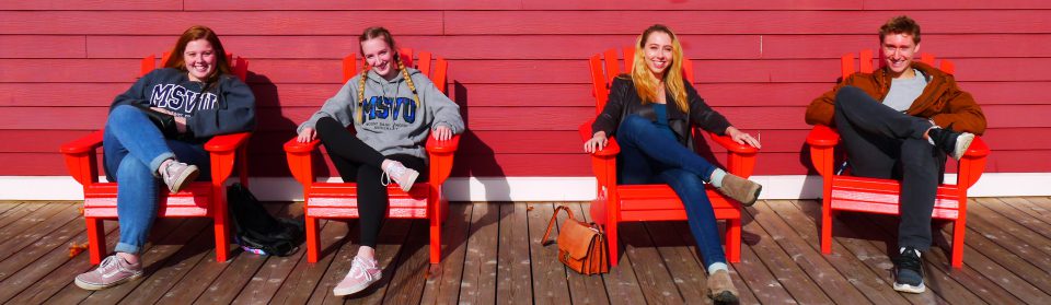 4 business and tourism students sitting in Adirondack chairs on a patio during one of the sustainable business tours.