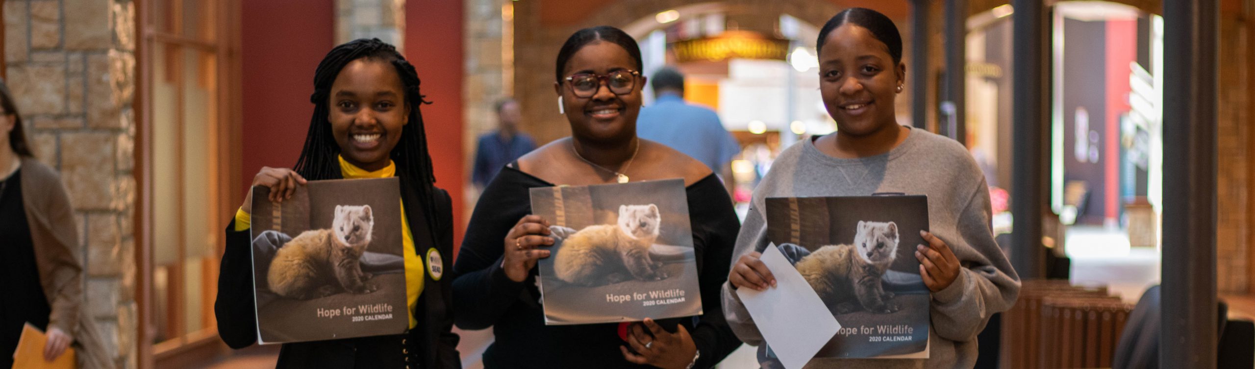Three Business and Tourism students holding the Hope for wildlife calendars that they are selling for their social enterprise during the 2020 SE4D event