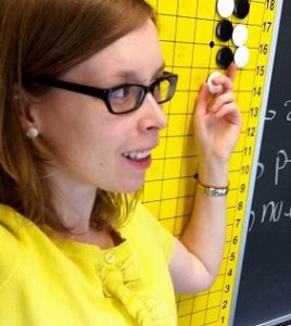 Dr. Danielle Cox, wearing a yellow blouse and pointing to a chalkboard