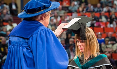 Student leaning forward having her degree conferred by official on the stage in Seton Academic Centre during the fall 2016 graduation ceremony