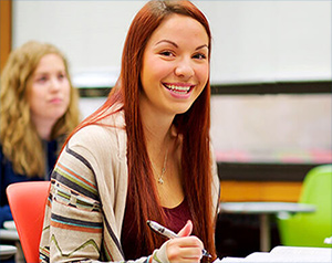 Student studying in classroom, smiling at the camera