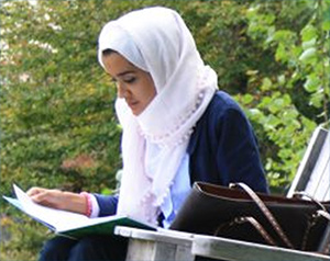Student wearing a hijab studying in a chair outside on campus