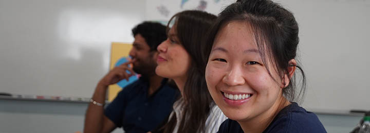 3 students in a classroom, one of the students is smiling at the camera.