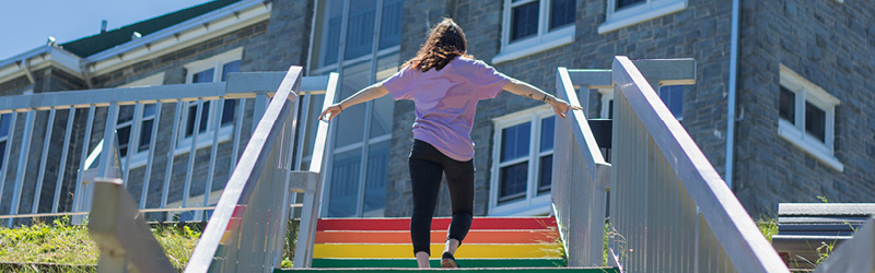 Student walking up Pride Stairs in front of Evaristus building