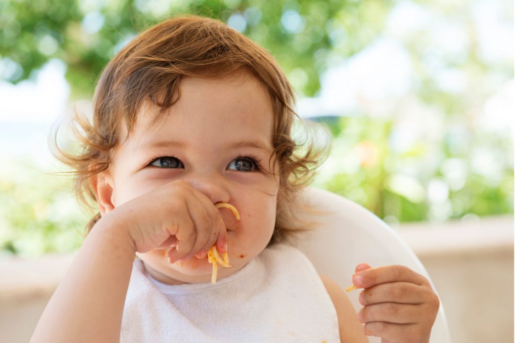 Alt= a toddler putting a handful of spaghetti in their mouth