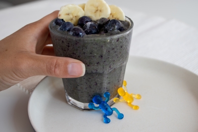 Hand holding blue smoothie in a glass with blueberries and slices of banana on top
