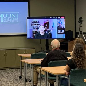 Brennan GooGoo appears on a television screen in front of a live audience