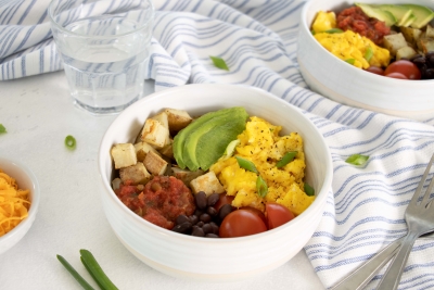Scrambled eggs, black beans, roasted potatoes, avocado, cherry tomatoes, and salsa in a white bowl