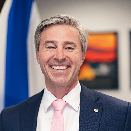 photo of tim houston smiling, wearing a navy suit and pink tie.