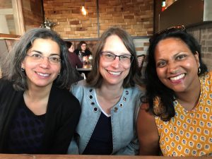 A photo of the three TMC Network Co-directors (from left to right: Maya Eichler, Tammy George and Nancy Taber). They are pictured shoulder-to-shoulder and smiling. 