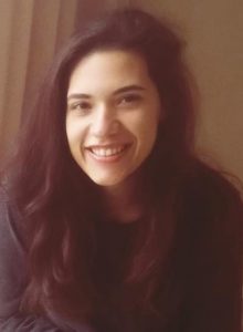 Photograph of Lea Aluie shows a smiling woman with long, dark hair and a black shirt looking directly at the camera.