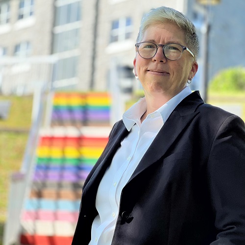 Dr. Joël Dickinson, standing in front of the Pride Stairs near Evaristus Hall