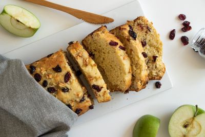 A partially sliced loaf of cranberry apple banana bread on a cutting board