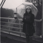 Emily Brown, holding an umbrella while standing near some train track
