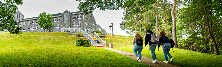 Three students walking up pathway to the pride stairs in front of Evaristus.