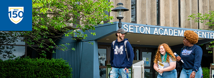 Students walking outside of the Seton Academic Centre with the 150th logo in the top left corner