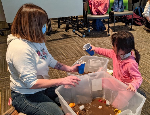 CHYS 3314: Play and Development: Infancy through Early Childhood student and a child pouring some dirt and mud into a cup