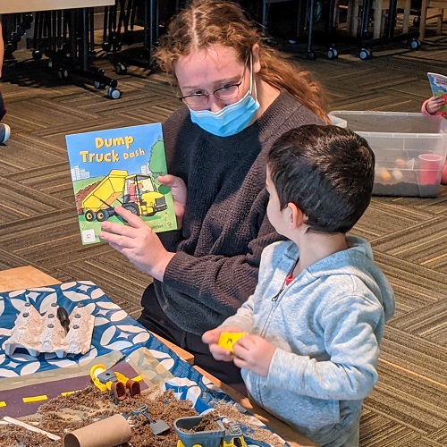 A Student from CHYS 3314 Play and Development: Infancy through Early Childhood course and a child from Child Study Centre looking a book about Dump Trucks