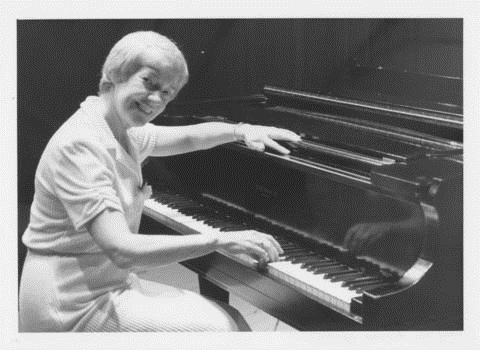 Sister Margaret posing beside a piano as she plays the piano keys