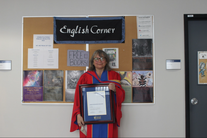 Anna Smol showing their Research Excellence Award in front of the English Corner sign